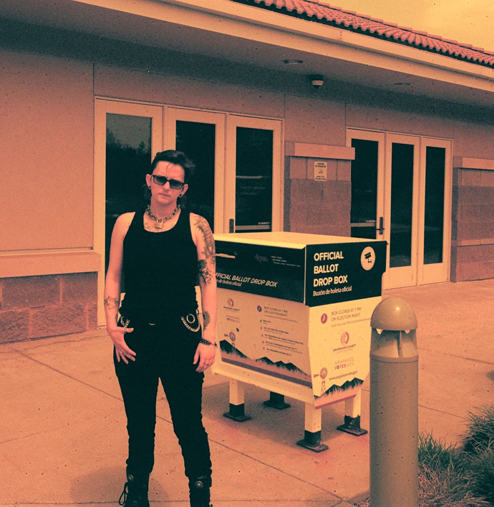 A faggot standing outside next to a ballot box.